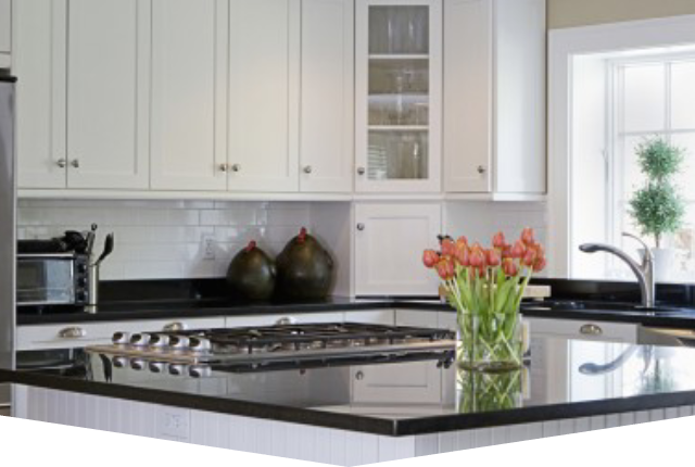 A kitchen with white cabinets and black counter tops.